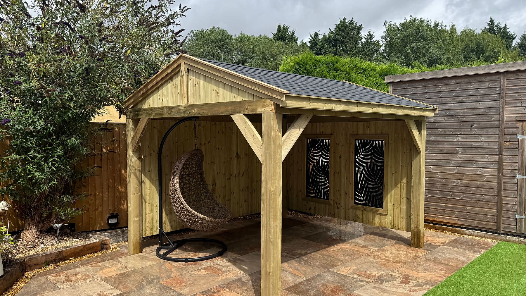 A handcrafted timber gazebo with decorative panels and an egg chair on a tiled patio