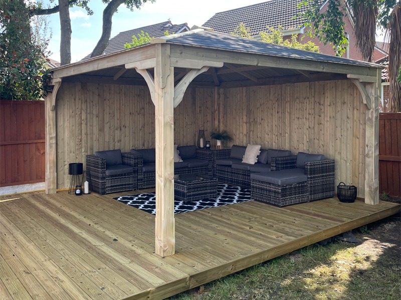 A timber gazebo with furnished seating in a garden