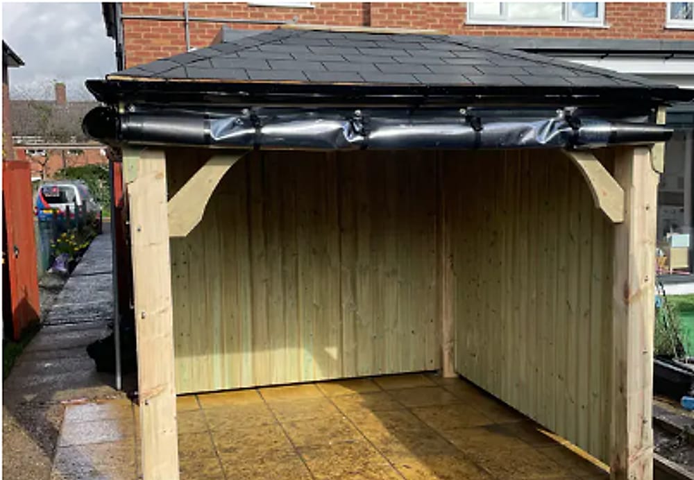 A timber gazebo with timber side panels fitted and a black rolled panel along the roof edge
