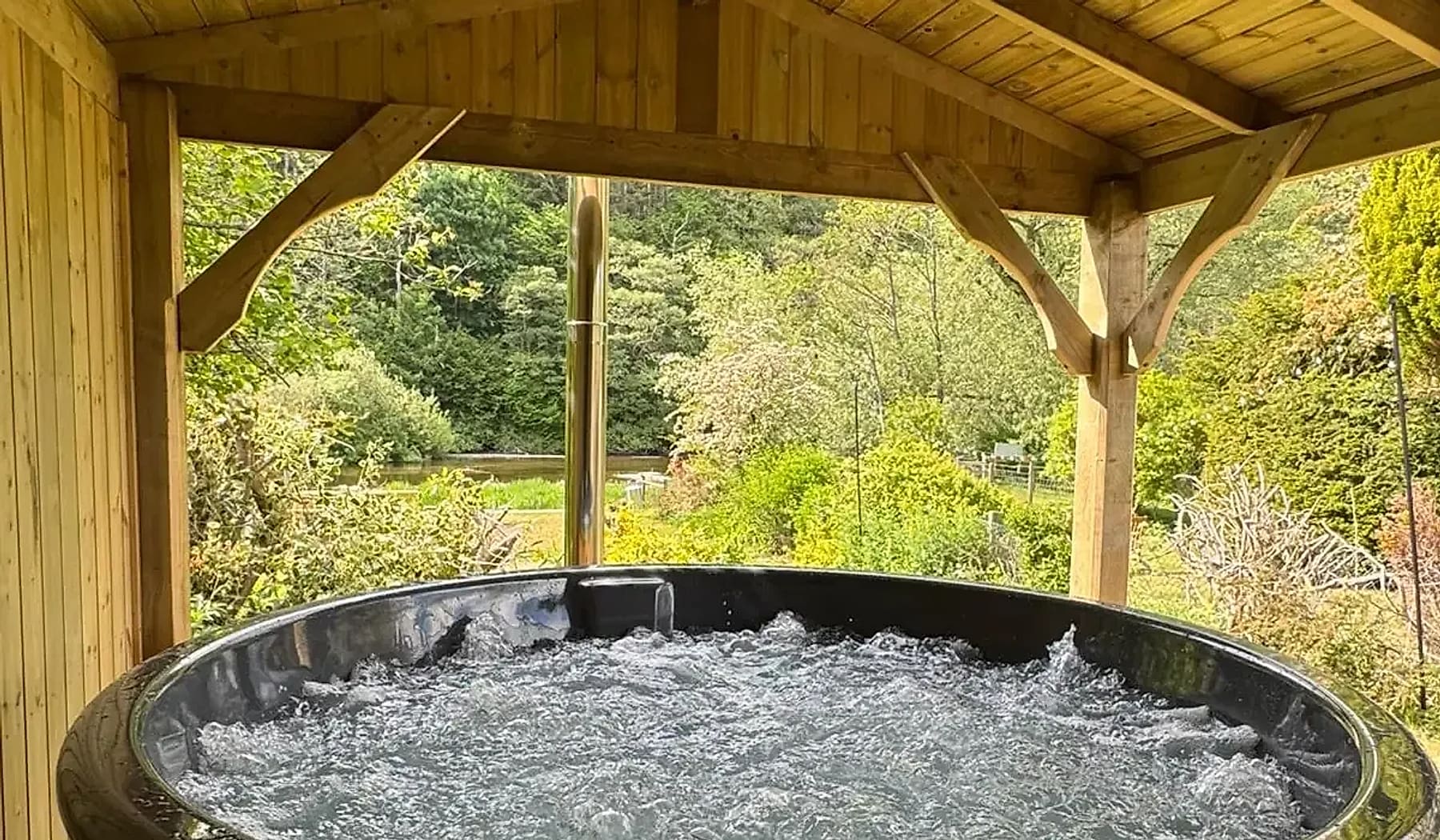 A bubbling hot tub beneath a timber gazebo with a view over the garden
