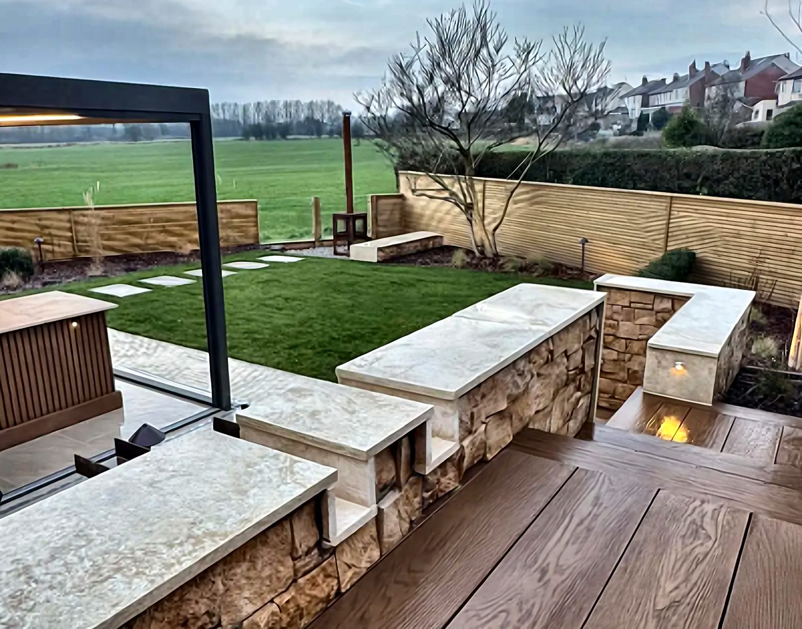 A landscaped garden with natural stone raised beds, a lawn and composite decking